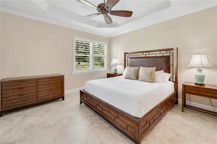 Bedroom with ceiling fan, a raised ceiling, light tile patterned flooring, and crown molding