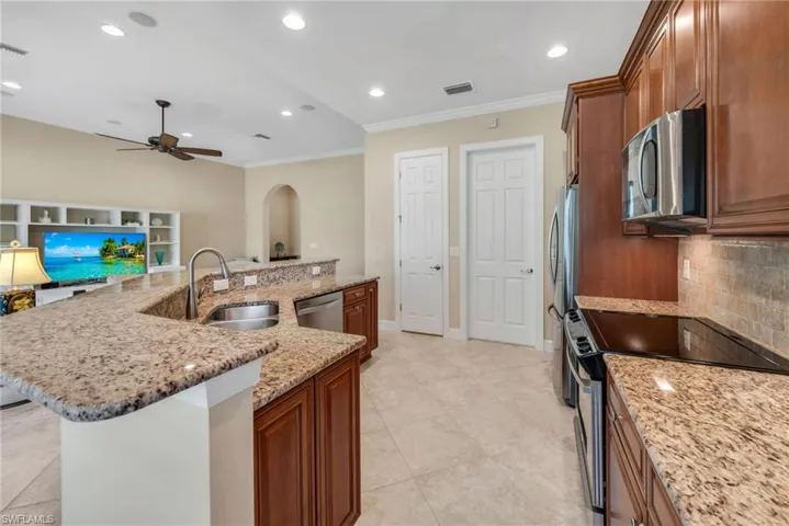 Kitchen featuring sink, a kitchen island with sink, stainless steel appliances, light stone countertops, and decorative backsplash