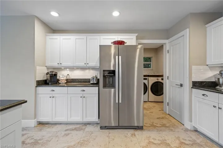 Kitchen featuring stainless steel refrigerator with ice dispenser, tasteful backsplash, washer and clothes dryer, white cabinets, and dark stone counters