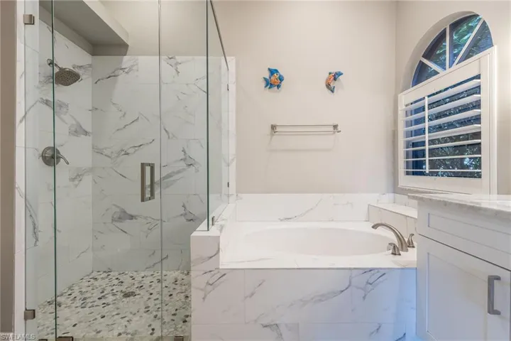 Full bath featuring a garden tub, a marble finish shower, and vanity