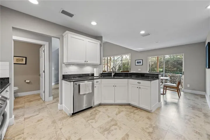 Kitchen with a peninsula, white cabinetry, dark stone counters, appliances with stainless steel finishes, and recessed lighting