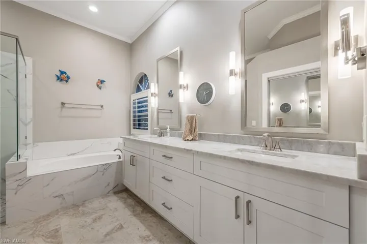 Full bathroom featuring double vanity, ornamental molding, a bath, and a marble finish shower