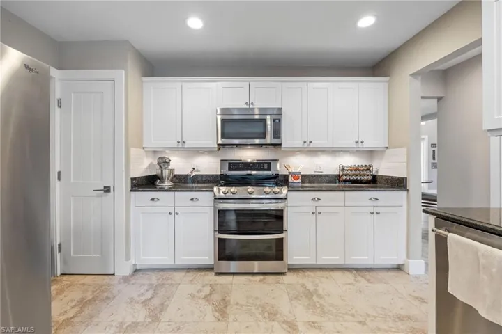 Kitchen with appliances with stainless steel finishes, white cabinetry, dark stone counters, and recessed lighting