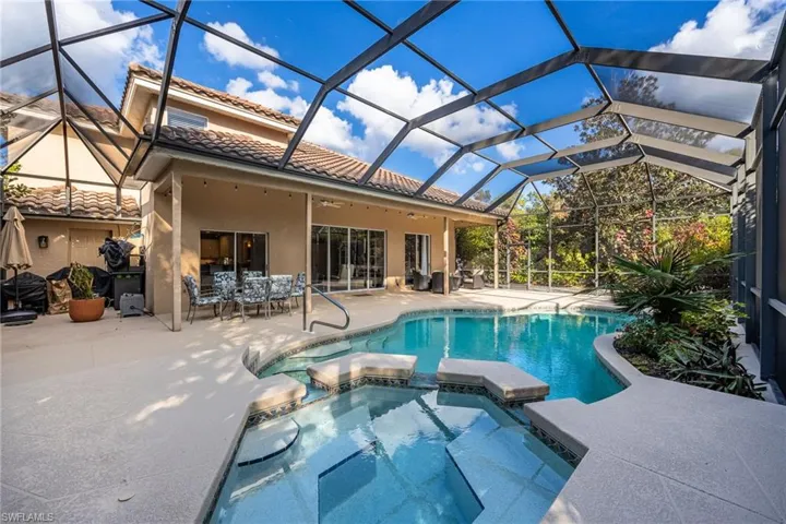 View of pool featuring a sunroom, a patio area, a pool with connected hot tub, glass enclosure, and outdoor dining area