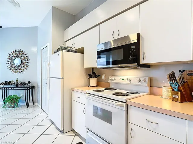 Kitchen with white appliances, white cabinetry, and light tile floors
