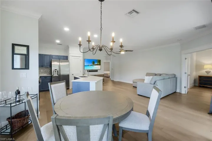 Open-concept living space featuring LVP flooring, a kitchen with blue cabinetry and stainless steel appliances, a central island with a white countertop, recessed lighting, and crown molding