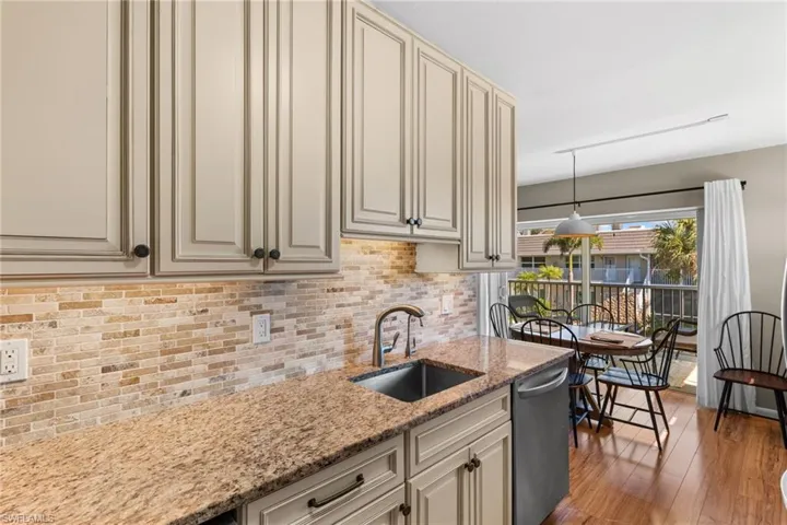 Kitchen featuring cream cabinets, light stone countertops, stainless steel dishwasher, and light wood-type flooring