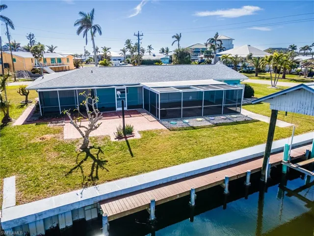 Back of property with a water view, a lawn, glass enclosure, and a patio area