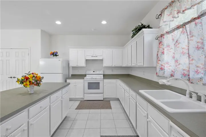 Kitchen with white cabinetry, white appliances, light tile patterned floors, recessed lighting, and under cabinet range hood