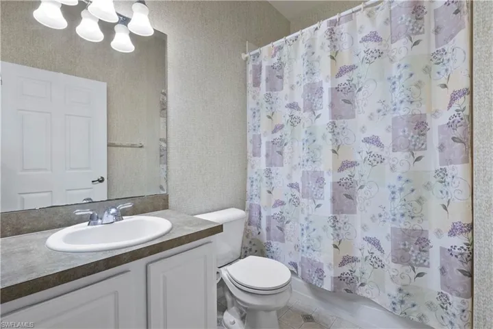 Bathroom featuring vanity, shower / tub combo with curtain, wallpapered walls, and tile patterned floors