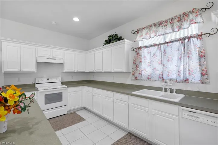 Kitchen featuring white appliances, light tile patterned flooring, white cabinetry, under cabinet range hood, and recessed lighting