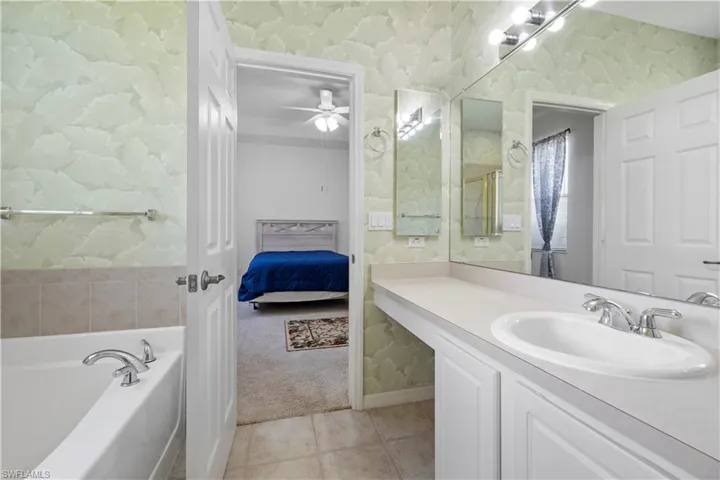Ensuite bathroom with wallpapered walls, vanity, light tile patterned flooring, a bath, and ceiling fan
