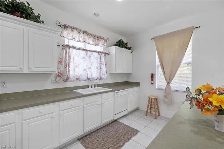 Kitchen with white cabinets, light tile patterned floors, dishwasher, and dark countertops