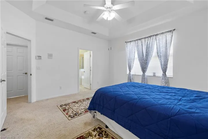 Bedroom with a raised ceiling, carpet flooring, ceiling fan, and connected bathroom