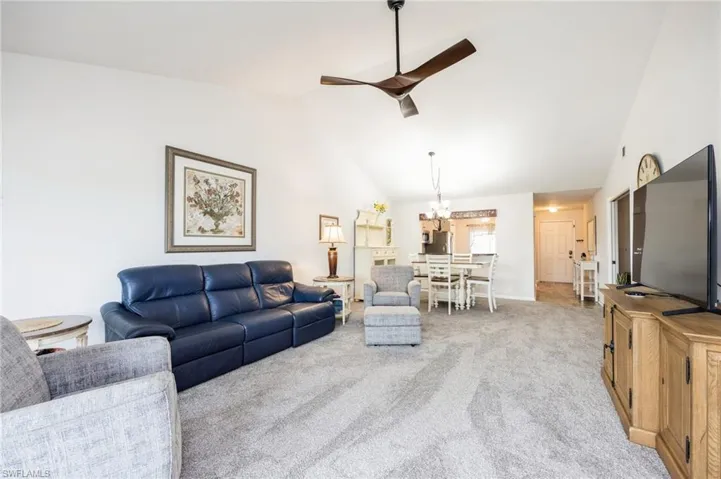 Carpeted living room with vaulted ceiling and ceiling fan with notable chandelier