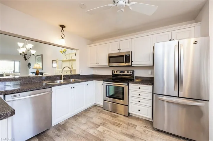 Kitchen with white cabinetry, hanging light fixtures, light hardwood / wood-style flooring, appliances with stainless steel finishes, and sink