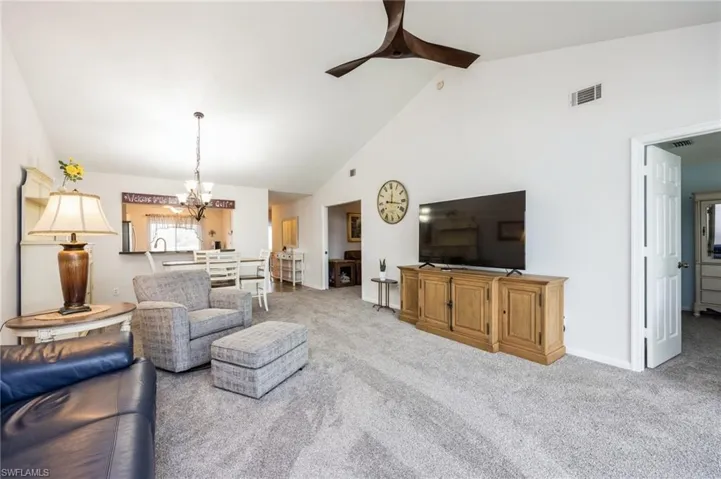 Living room featuring high vaulted ceiling, light carpet, sink, and ceiling fan with notable chandelier
