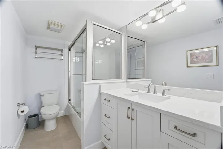 Bathroom with vanity, bath / shower combo with glass door, and light tile patterned floors