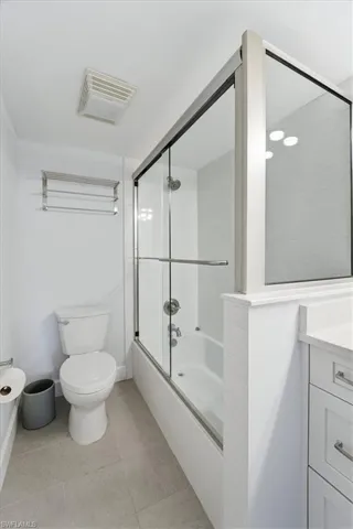 Bathroom with bath / shower combo with glass door, vanity, and light tile patterned floors