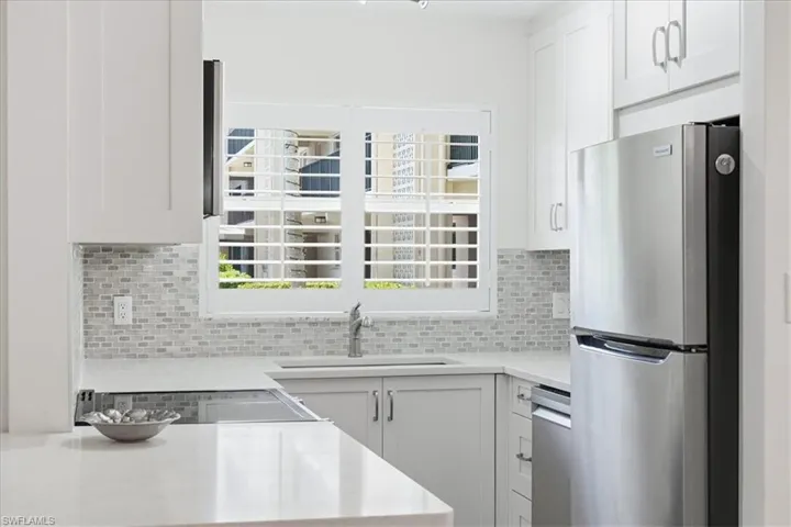 Kitchen with stainless steel appliances, white cabinets, light stone counters, and tasteful backsplash