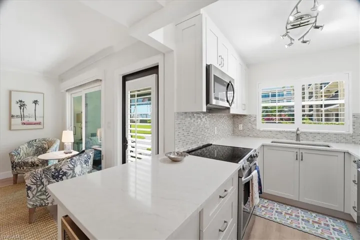 Kitchen with appliances with stainless steel finishes, light stone counters, tasteful backsplash, white cabinets, and crown molding