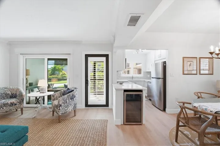 Kitchen with beverage cooler, white cabinets, stainless steel appliances, light wood-style flooring, and tasteful backsplash