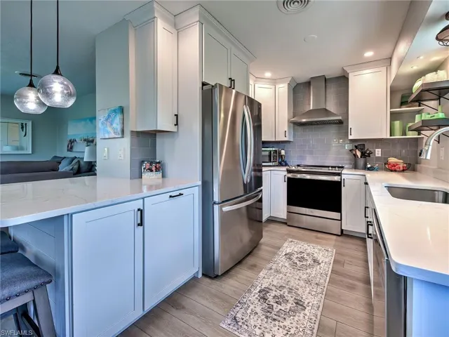 Kitchen with a peninsula, light stone counters, stainless steel appliances, and open shelves