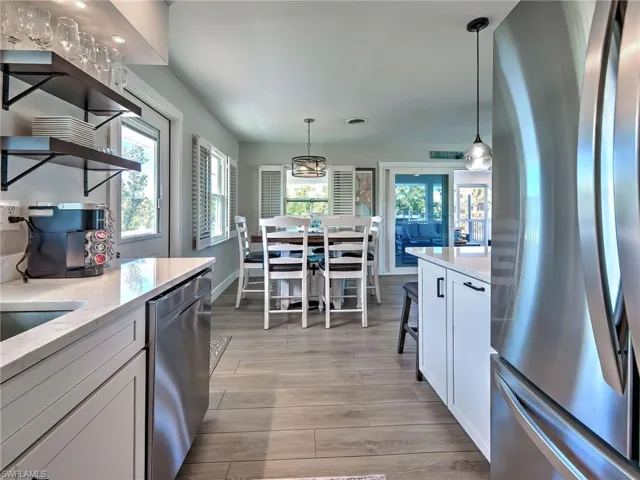 Kitchen with stainless steel appliances, light stone countertops, white cabinetry, light wood-style floors, and hanging light fixtures