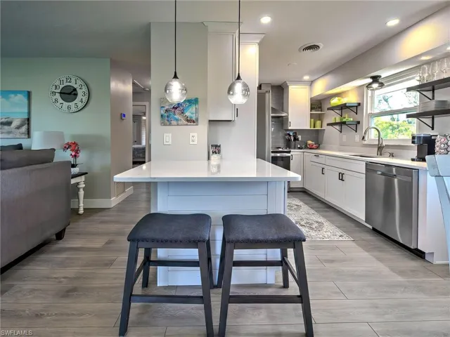 Kitchen featuring stainless steel appliances, white cabinets, pendant lighting, backsplash, and light wood-style flooring
