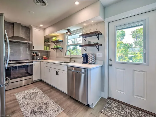 Kitchen with white cabinetry, open shelves, stainless steel appliances, light wood-style flooring, and light stone counters