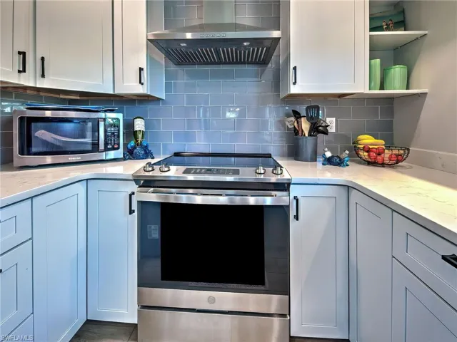 Kitchen with stainless steel appliances, light stone counters, white cabinets, and tasteful backsplash