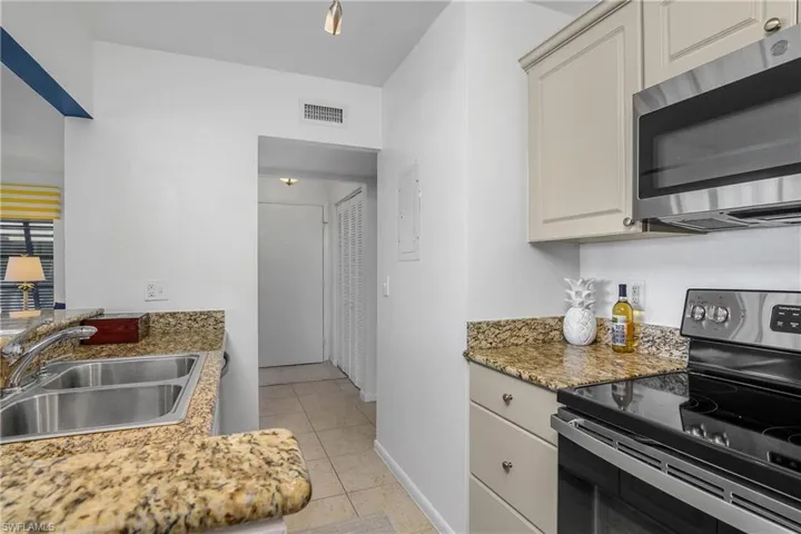 Kitchen featuring granite countertops, sink, light tile patterned floors, and appliances with stainless steel finishes.
