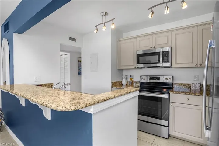 Kitchen featuring a kitchen bar, decorative light fixtures, kitchen peninsula, stainless steel appliances, and cream cabinetry.