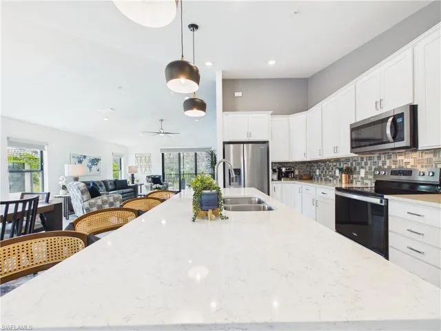 Kitchen with stainless steel appliances, decorative light fixtures, white cabinetry, tasteful backsplash, and light stone countertops