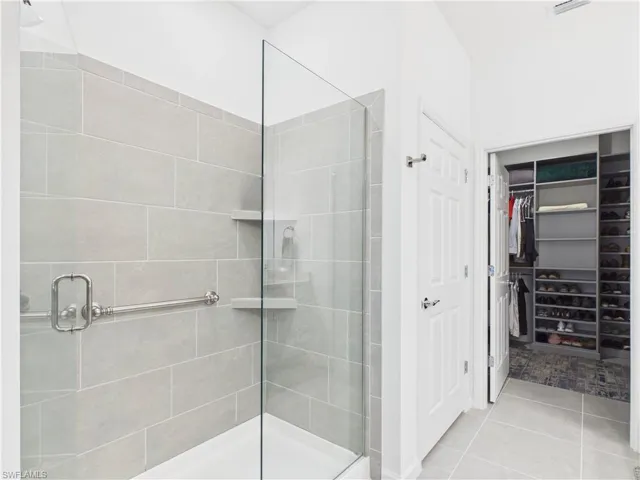 Full bathroom featuring a shower stall, a spacious closet, and light tile patterned floors