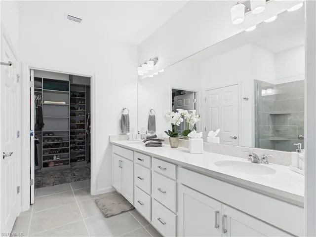Bathroom featuring double vanity, a stall shower, light tile patterned floors, and a spacious closet