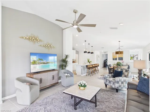 Living room featuring a ceiling fan, vaulted ceiling, and light tile patterned flooring