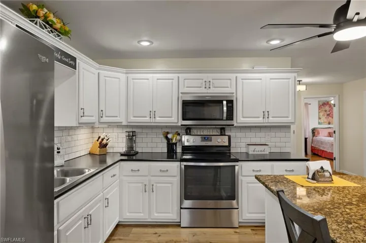 Kitchen featuring light hardwood / wood-style flooring, white cabinets, ceiling fan, stainless steel appliances, and backsplash