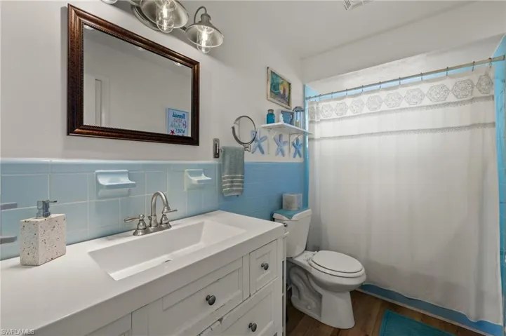 Bathroom with toilet, tile walls, vanity, a shower with shower curtain, and hardwood / wood-style flooring
