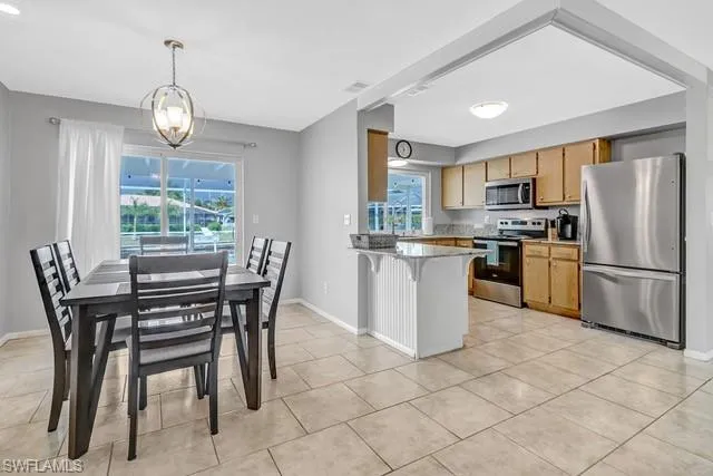 Kitchen with stainless steel appliances, a peninsula, a kitchen breakfast bar, light stone countertops, and suspended lighting