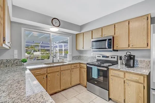 Kitchen featuring stainless steel appliances, light stone counters, light tile patterned floors, and light wood finish cabinetry