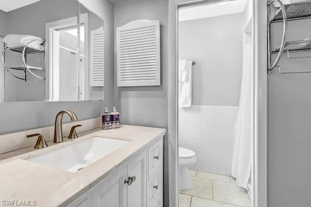 Full bath featuring vanity, tile walls, curtained shower, wainscoting, and light tile patterned floors