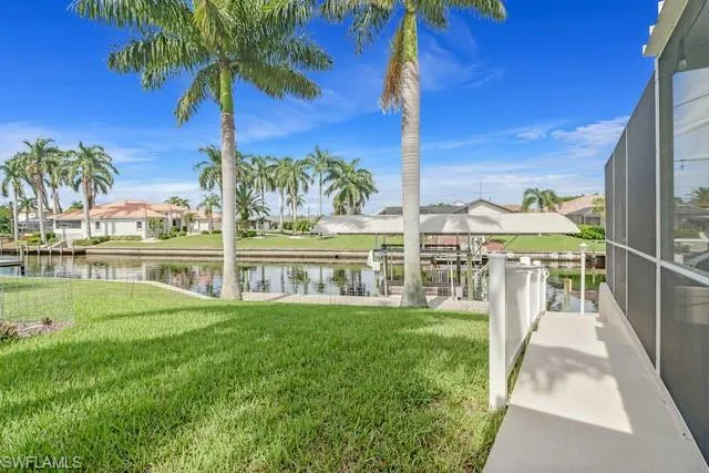 View of grassy yard with boat lift, a dock, a lanai, a water view, and a sunroom