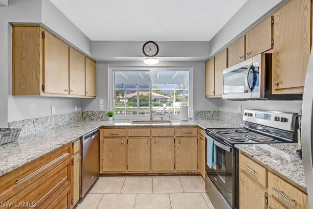 Kitchen featuring stainless steel appliances, light stone counters, light tile patterned floors, and light wood finish cabinetry