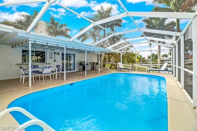 Outdoor pool featuring glass enclosure, a sunroom, a patio, outdoor dining area, and grilling area
