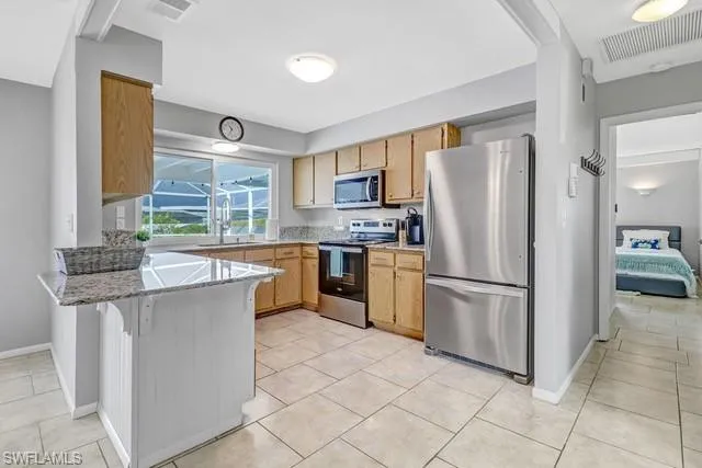 Kitchen with stainless steel appliances, a peninsula, light stone counters, a kitchen breakfast bar, and light tile patterned flooring