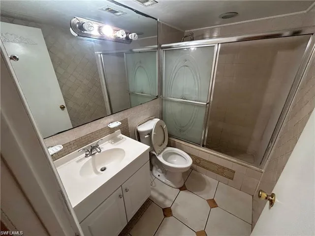 Bathroom with vanity, tiled shower, tile walls, and tile patterned flooring