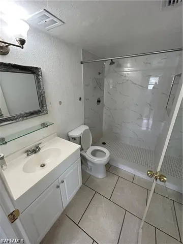 Bathroom featuring a marble finish shower, vanity, a textured wall, and a textured ceiling