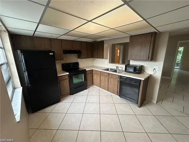 Kitchen with black appliances, light countertops, a drop ceiling, and light tile patterned floors