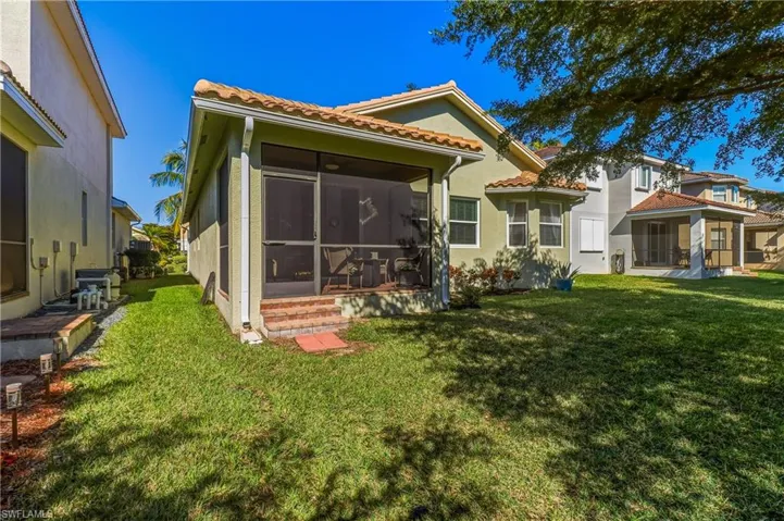 Back of house with a sunroom, a lawn, a tiled roof, and stucco siding